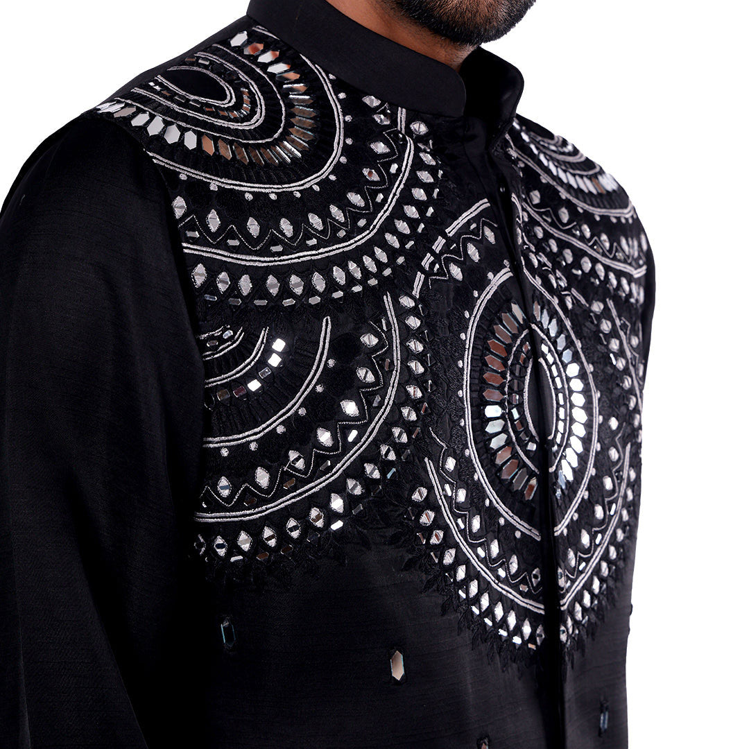 Macro detail of the black Nehru jacket shoulder: bold ornamental mirror-work pattern with Resham embroidery