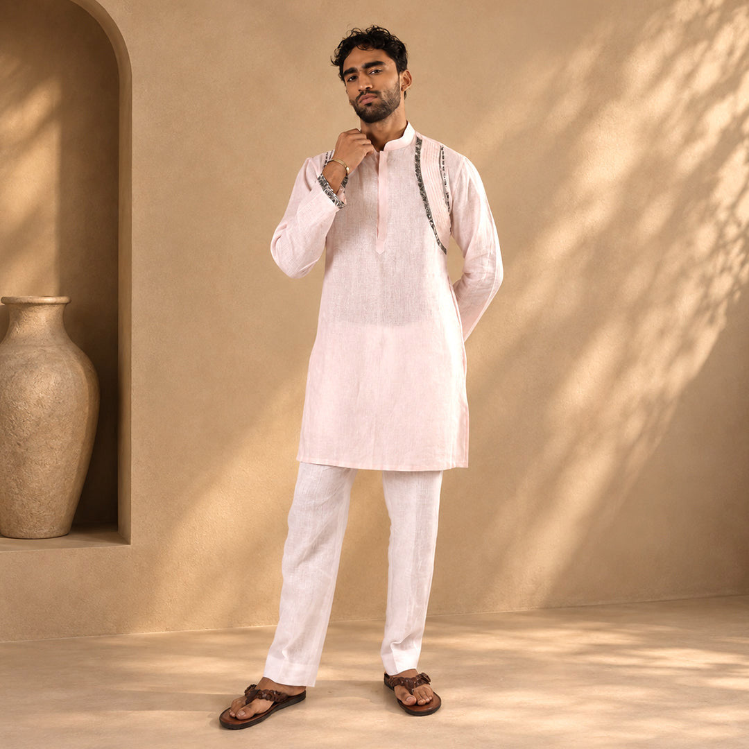 Powder Pink Linear-Accent Linen Kurta Set with white trousers, model in a beige set beside a stone urn
